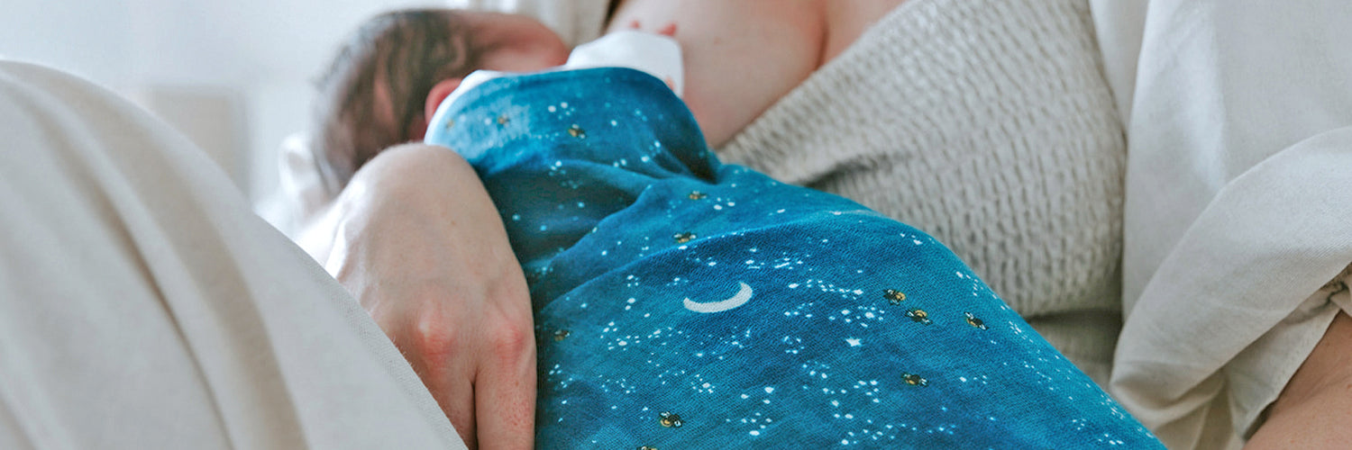 Mother feeding baby in dark blue starry night swaddle