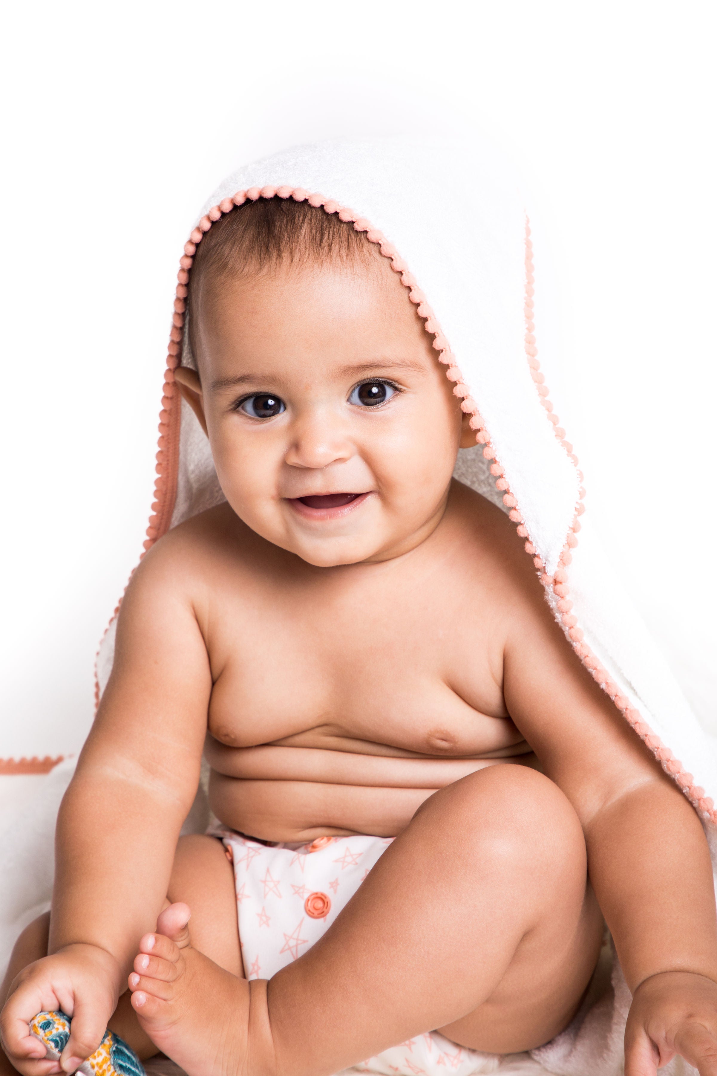 malabar baby white bamboo cotton towel shown on a cute and happy baby. The towel is white and silky soft and has a hood. The towel also has a detailed pom pom trim. The towel is extra large and fits newborns - toddlers 5 years old. Pom Pom colors are show