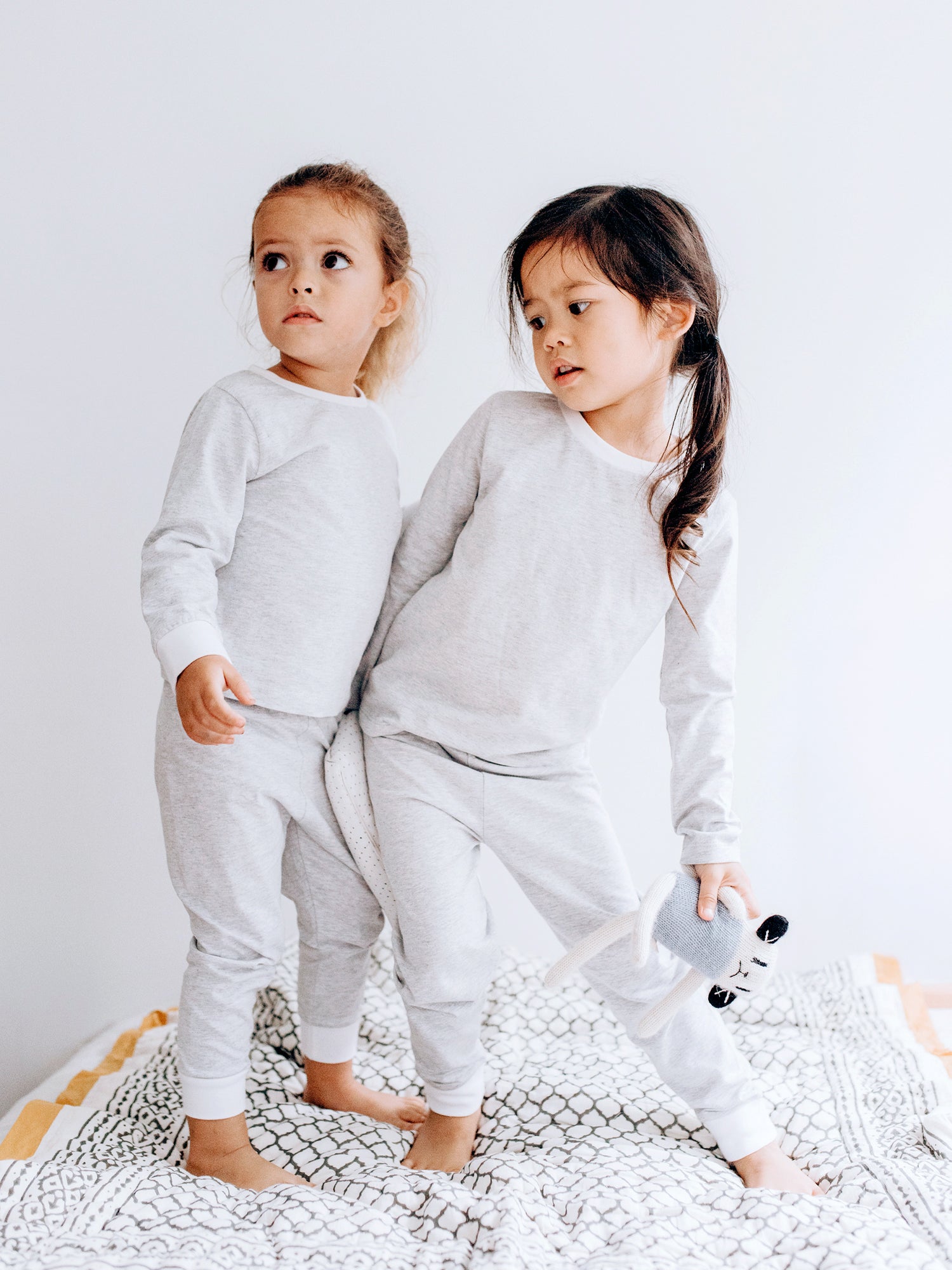 Two children wearing gray pajamas standing on a white background